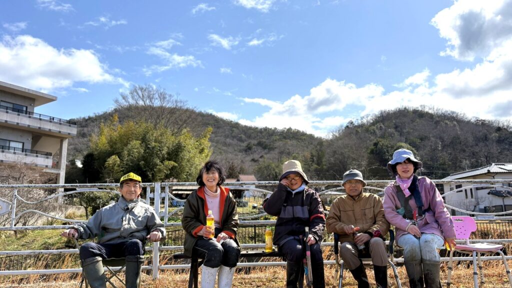 蛍の生息地整備活動後に並んで座る環境部会メンバー5名