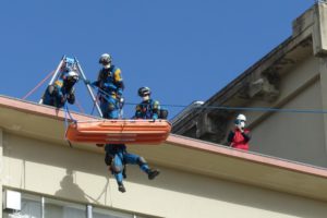 校舎の屋上に5人ほどがいる。ロープを設置しており、今まさにボートに載せた人と消防士が一人、屋上から降りてこようとしている。